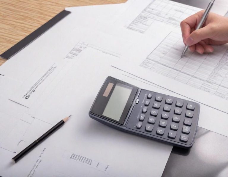 Händeschreiber an Dokumenten mit einem Taschenrechner und einem Stift.