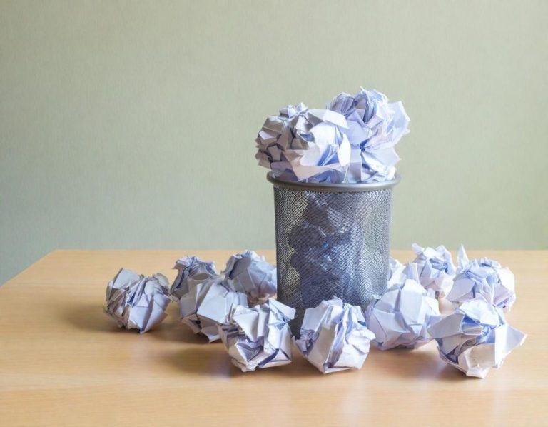 Ein Papierkorb mit zerknülltem Papier und einige Papiere auf einem Tisch verteilt.