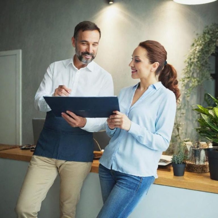 Ein Mann und eine Frau stehen an einem Empfangstresen und besprechen Unterlagen.